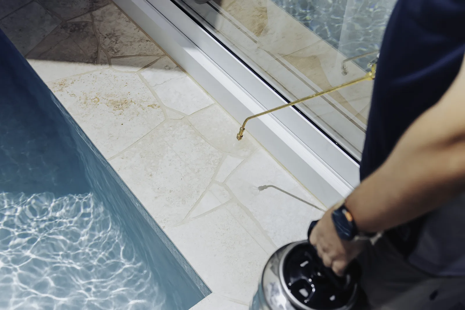 Certified applicator spray-sealing natural stone paving beside a pool
